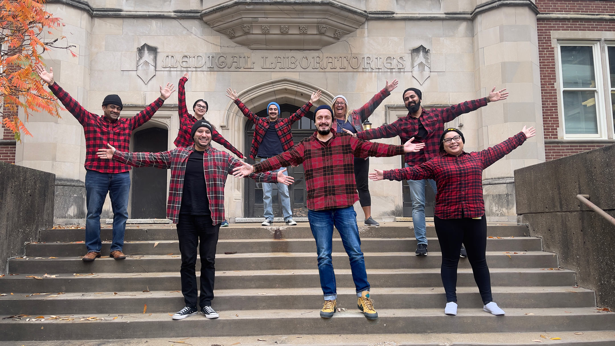 Lab members and Dr. Badovinac posing on the Medical Laboratories with their arms outstretched and they're all wearing red plaid flannel shirts