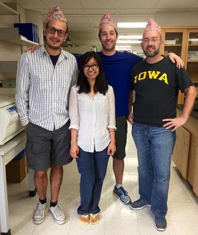 Four lab members smiling, three of them are wearing party hats