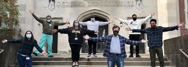 Lab members standing with arms outstretched, wearing masks outside of the Medical Laboratories