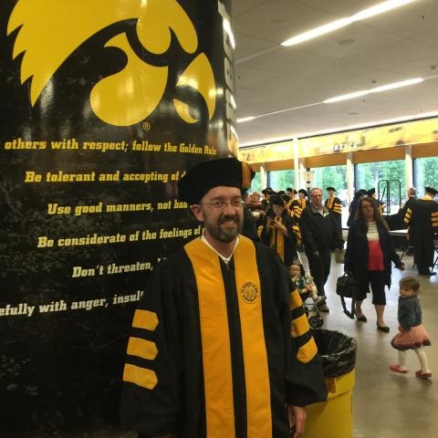 A person in a graduation gown standing in front of the Tigerhawk logo
