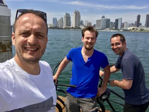 Three people smiling outside near a body of water