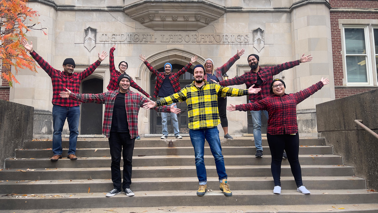 Lab members and Dr. Badovinac posing on the Medical Laboratories with their arms outstretched and they're all wearing red plaid flannel shirts