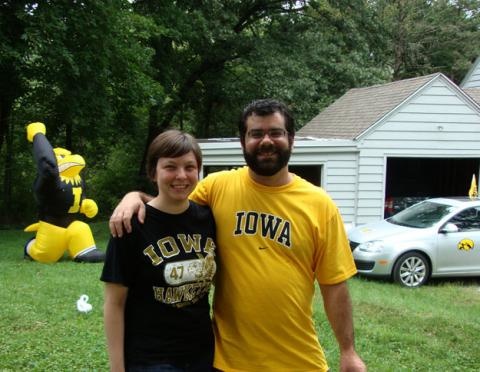 Two people outside smiling with a car that has a Tigerhawk decal in thebackground