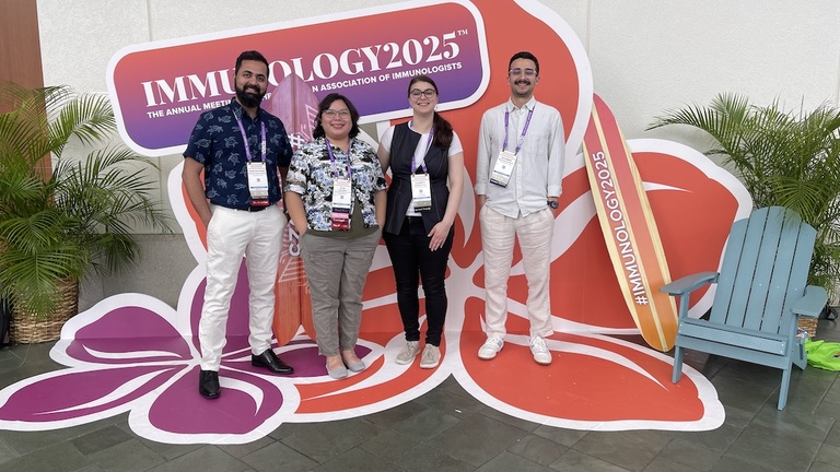 four people standing in front of a flower-shaped conference sign smiling