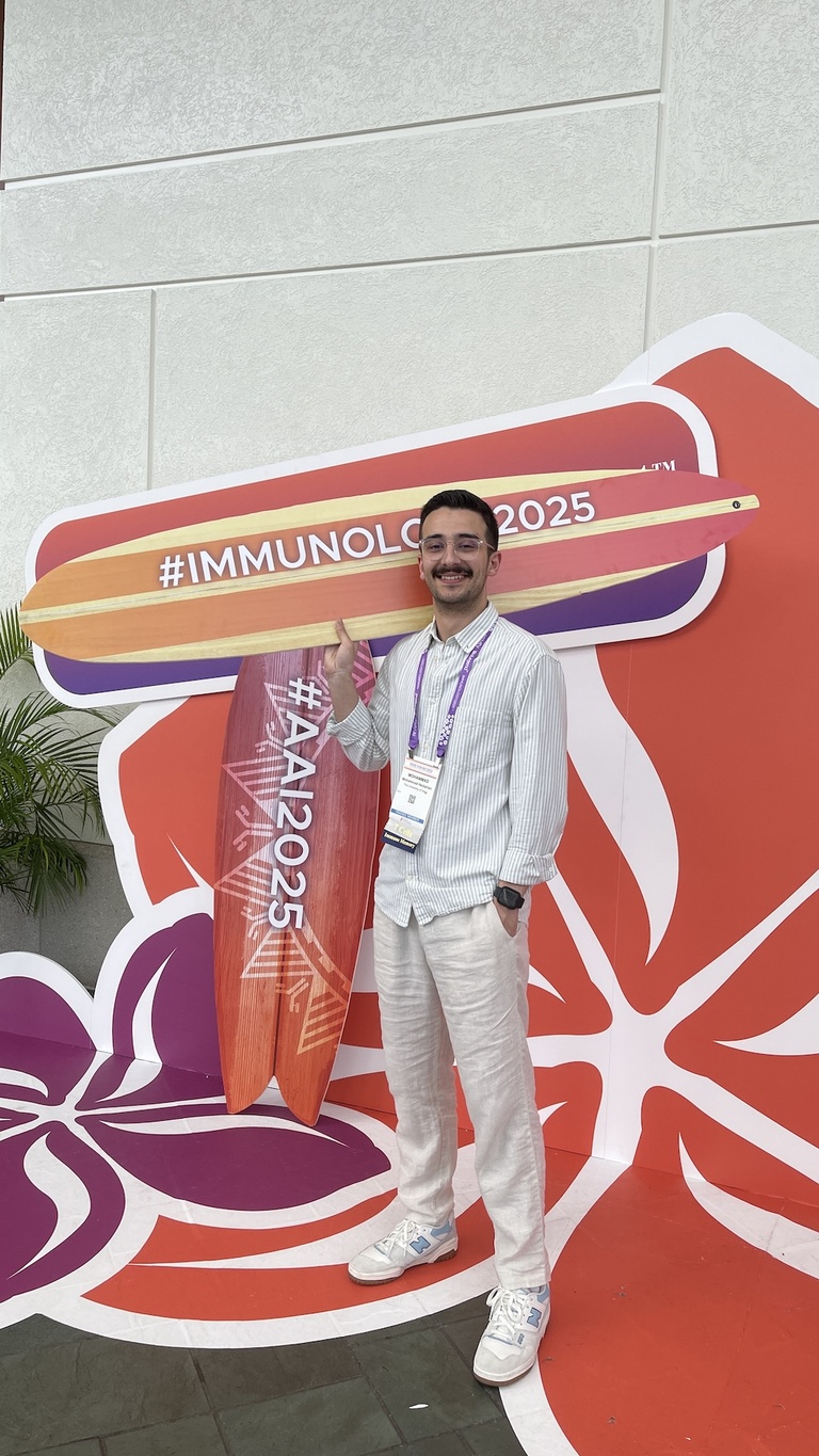 A person holding a surfboard in front of a flower-shaped conference sign