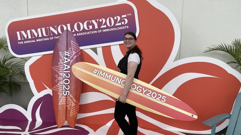 A person holding a surfboard in front of a flower-shaped conference sign