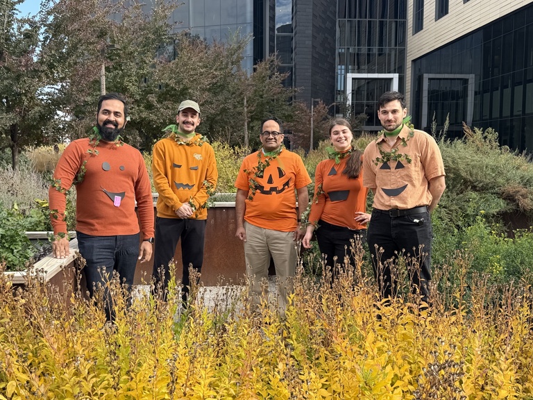 Lab Members wearing pumpkin shirts popping out of some plants