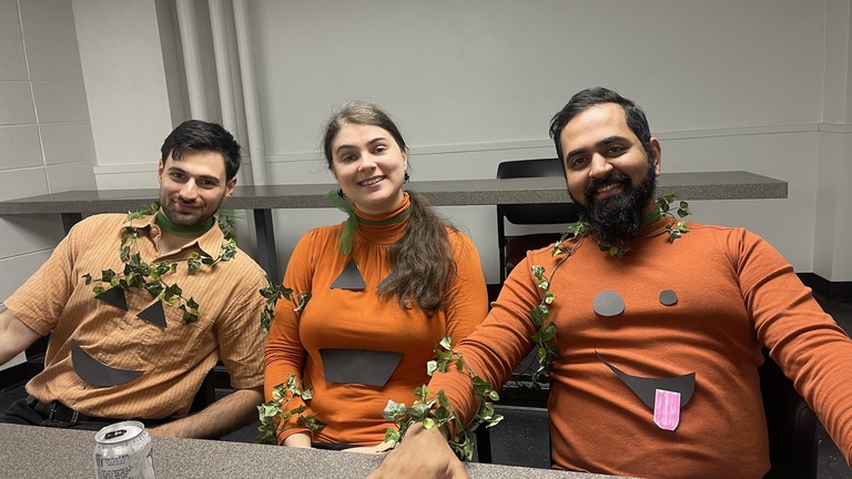 Lab Members wearing pumpkin shirts popping out of some plants